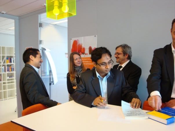 Harish Kumar at a Duisenberg School of Finance event, signing documents at a table with orange chairs and faculty